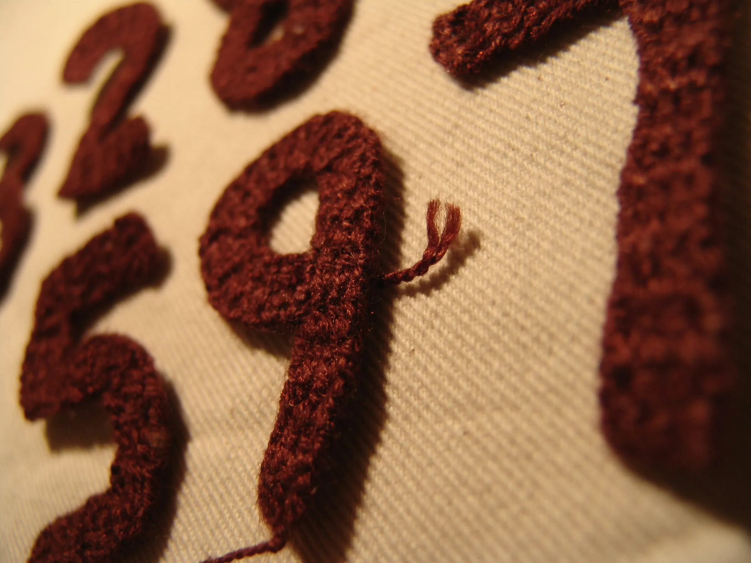 Macro of burgundy chenille varsity numerals stitched onto cream twill