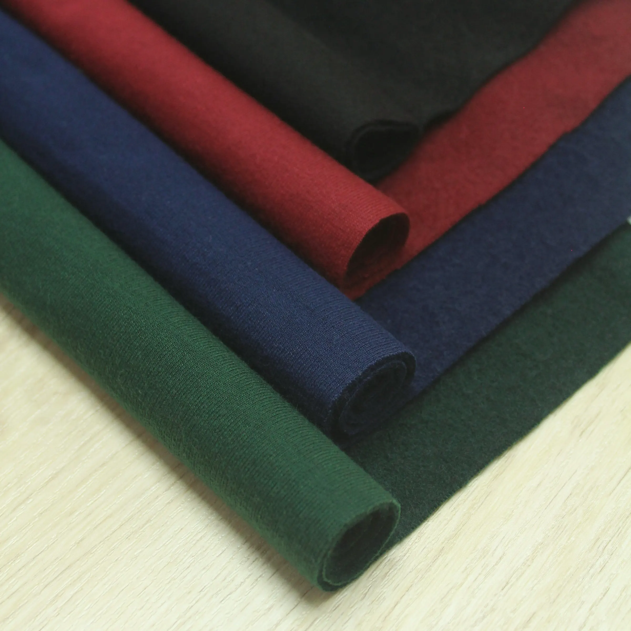 Rolled cotton fabric in forest green, navy and burgundy on a pale wood table
