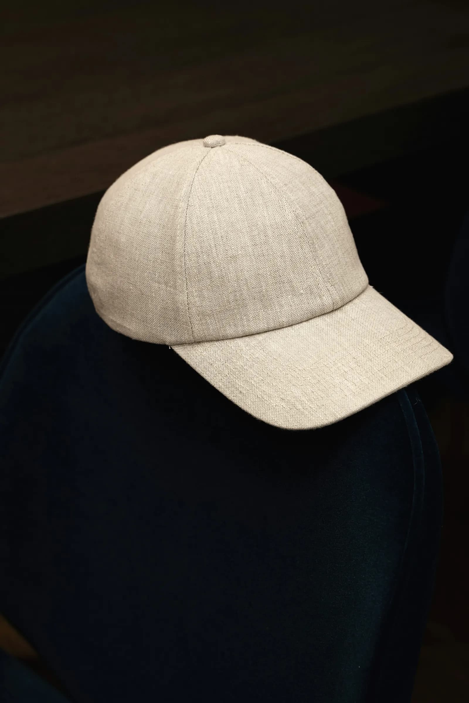 An unbranded natural-linen six-panel dad hat resting on a dark navy surface in low light