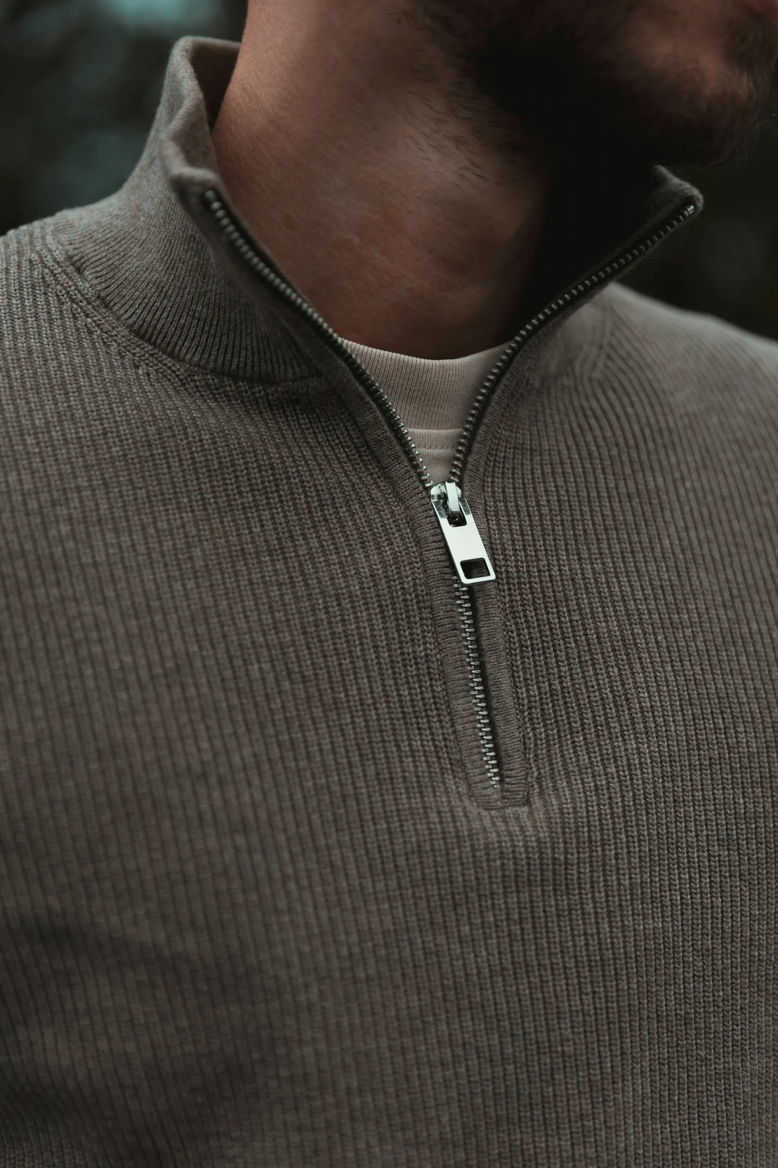 Close-up of a taupe rib-knit quarter-zip pullover with a metal zip, worn over a cream tee